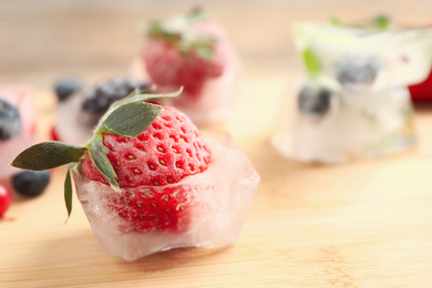 Ice cube with frozen strawberry on wooden table, closeup. Space for text