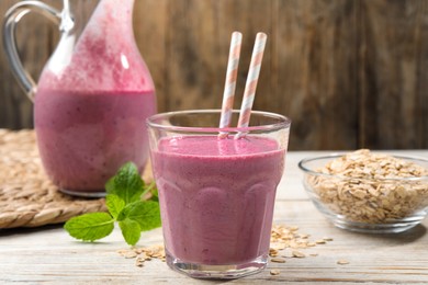Glass of blackberry smoothie with straws, mint and oatmeal on light wooden table