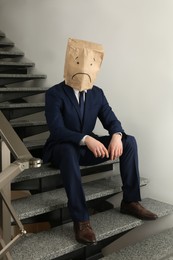 Man wearing paper bag with drawn sad face indoors