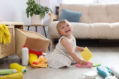 Photo of Cute baby playing with cleaning supplies on floor at home. Dangerous situation