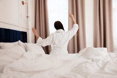 Young woman wearing bathrobe waking up in hotel room, back view