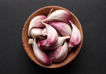 Photo of Unpeeled garlic cloves in wooden bowl on black background, top view