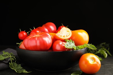 Many different ripe tomatoes with leaves on black table