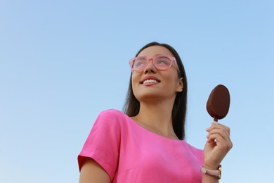 Beautiful young woman holding ice cream glazed in chocolate against blue sky, low angle view