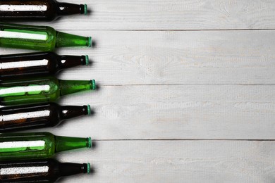 Photo of Glass bottles of beer on grey wooden background, flat lay. Space for text