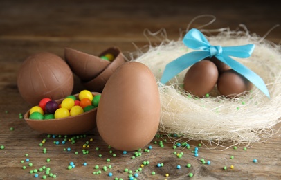 Composition with tasty chocolate eggs, colorful candies and decorative nest on wooden table