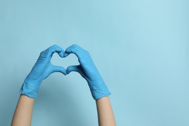 Photo of Doctor in medical gloves making heart with hands on light blue background, closeup. Space for text