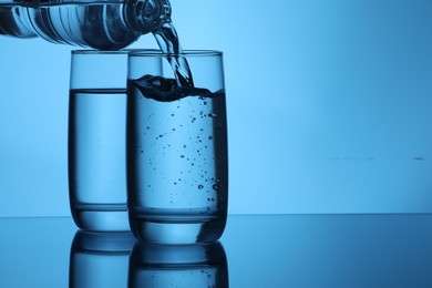Photo of Pouring water from bottle into glass on light blue background. Space for text