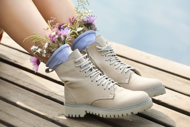 Woman sitting on wooden pier with flowers in socks outdoors, closeup