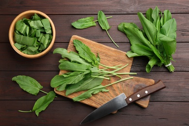 Fresh green sorrel leaves and knife on brown wooden table, flat lay