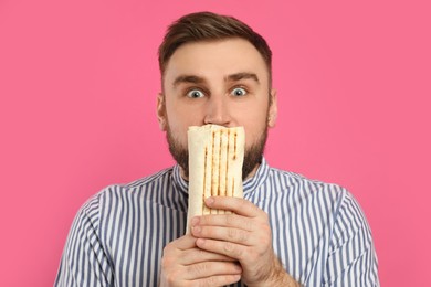 Photo of Emotional young man with delicious shawarma on pink background