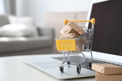 Internet shopping. Laptop and small cart with boxes on table indoors, space for text