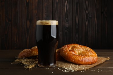 Tasty pretzels, glass of beer and wheat spikes on wooden table