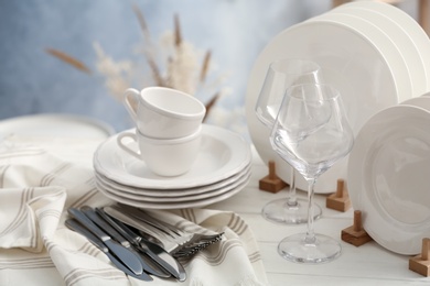 Photo of Set of clean dishware, cutlery and wineglasses on white wooden table