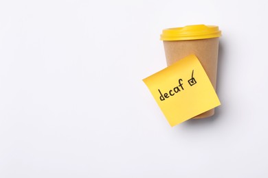 Note with word Decaf and checkbox attached to takeaway coffee cup on white background, top view. Space for text