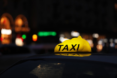 Taxi car with yellow checkered sign on city street in evening, closeup