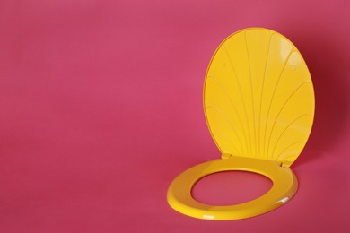 New yellow plastic toilet seat on pink background, space for text