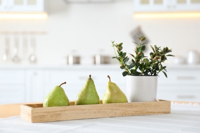 Fresh ripe pears and plant on table in kitchen