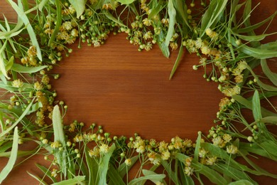 Frame of beautiful linden blossoms and green leaves on wooden table, flat lay. Space for text