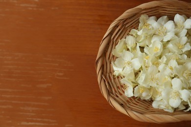Beautiful white jasmine flowers in wicker basket on wooden table, top view. Space for text