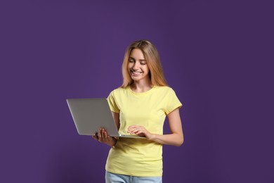 Photo of Portrait of young woman with modern laptop on purple background