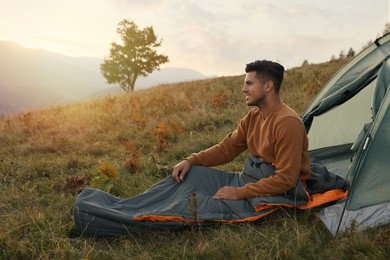 Man in sleeping bag near camping tent on hill