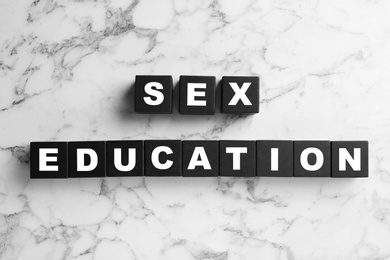 Black wooden blocks with phrase "SEX EDUCATION" on marble background, flat lay
