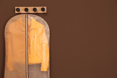 Photo of Garment bag with jacket hanging on brown wall. Space for text