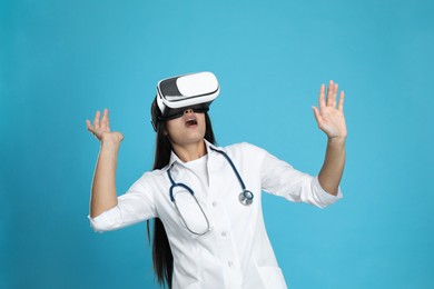 Emotional female doctor using virtual reality headset on light blue background