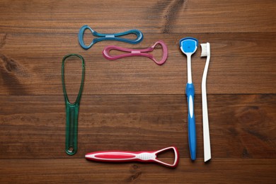 Frame of different tongue cleaners and toothbrush on wooden table, flat lay. Space for text