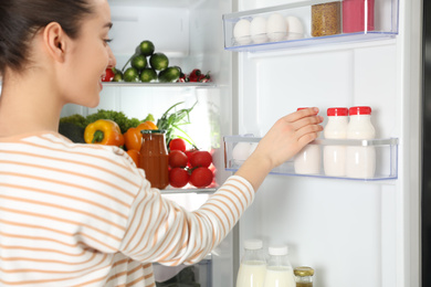 Young woman taking yoghurt out of refrigerator, closeup