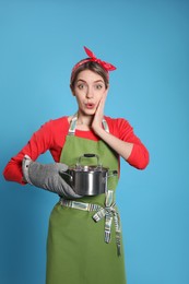 Young housewife with pot on light blue background