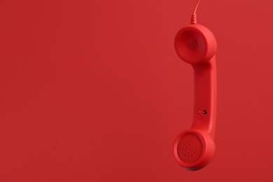 Corded telephone handset hanging on red background, space for text. Hotline concept