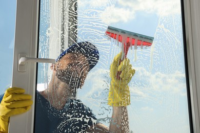 Photo of Man cleaning glass with squeegee indoors, view from inside