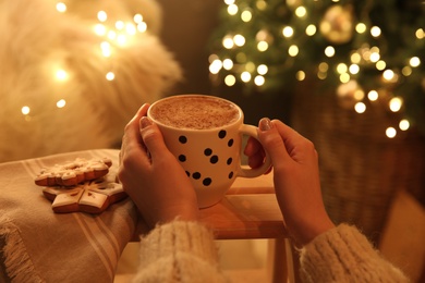 Woman with cup of hot drink and Christmas cookies at home, closeup