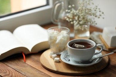 Tray with cup of freshly brewed tea and sugar cubes on wooden table, space for text