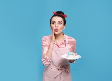 Photo of Young housewife with tasty cupcake on light blue background