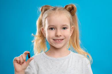 Photo of Little girl with vitamin pill on blue background