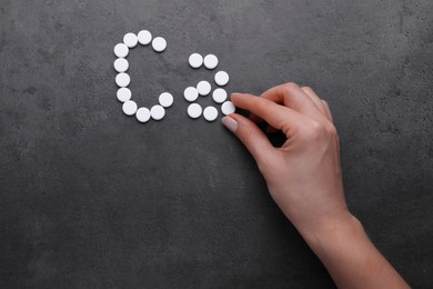 Woman making symbol Ca (Calcium) of pills on black background, top view
