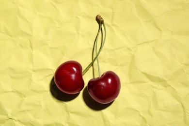 Sweet red cherries on creased yellow paper, top view