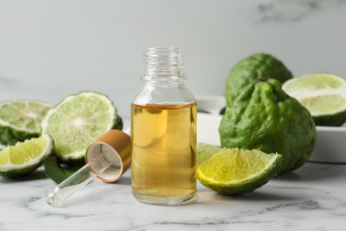 Photo of Bottle of essential oil, pipette and fresh bergamot fruits on white marble table