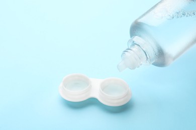 Photo of Dripping solution into case with contact lenses on light blue background, closeup. Space for text