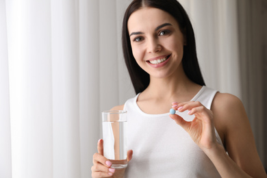 Young woman with glass of water and vitamin pill on light background. Space for text