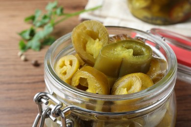 Photo of Glass jar with slices of pickled green jalapeno peppers on wooden table, closeup