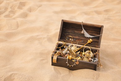 Photo of Open wooden treasure chest on sand, space for text