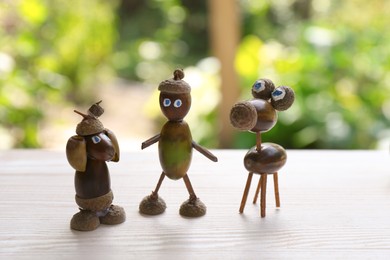 Photo of Cute figures made of acorns on white wooden table