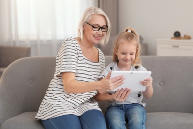 Portrait of mature woman and her granddaughter using tablet together in living room