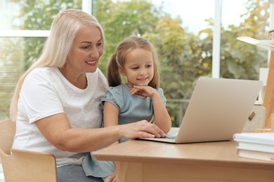 Photo of Happy grandmother and her granddaughter using laptop together at home