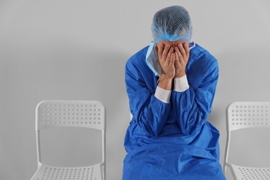 Exhausted doctor sitting on chair near grey wall, space for text