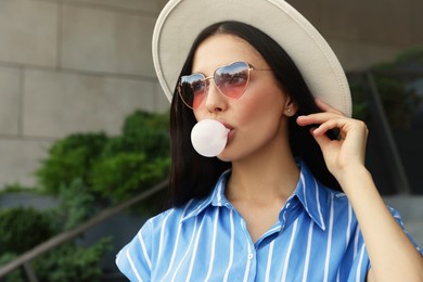 Photo of Stylish woman blowing gum near building outdoors